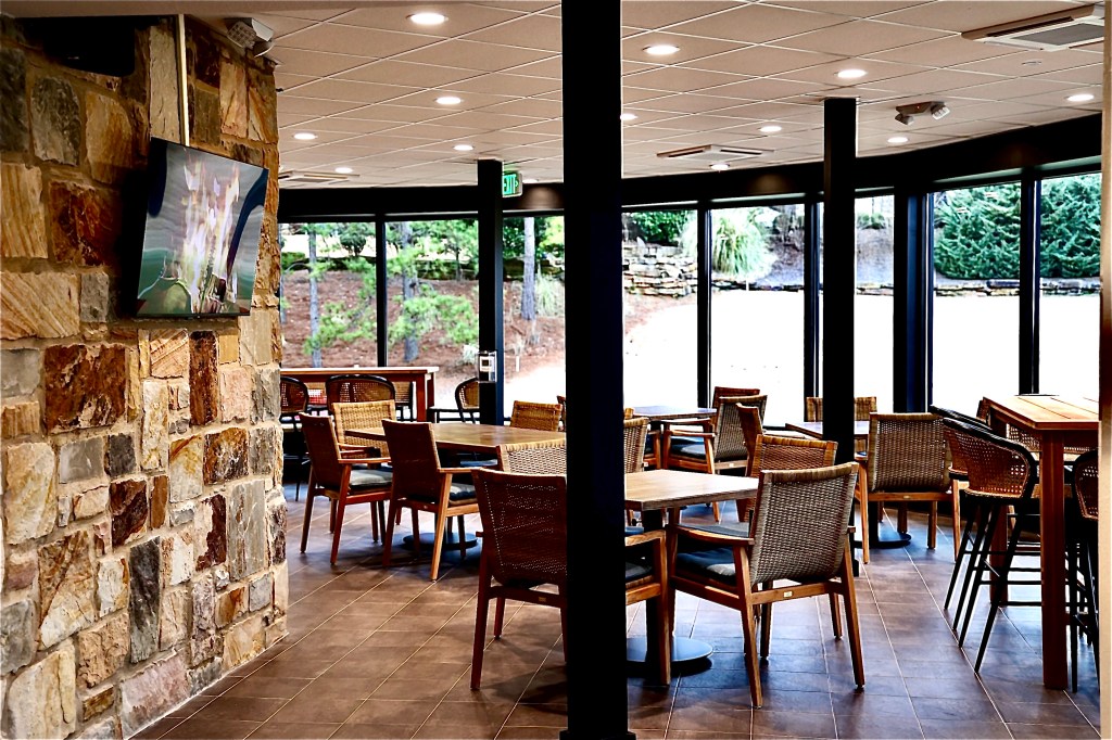 View of dining area from the front, brown interior with tables and chairs throughout. Window walls in the background.